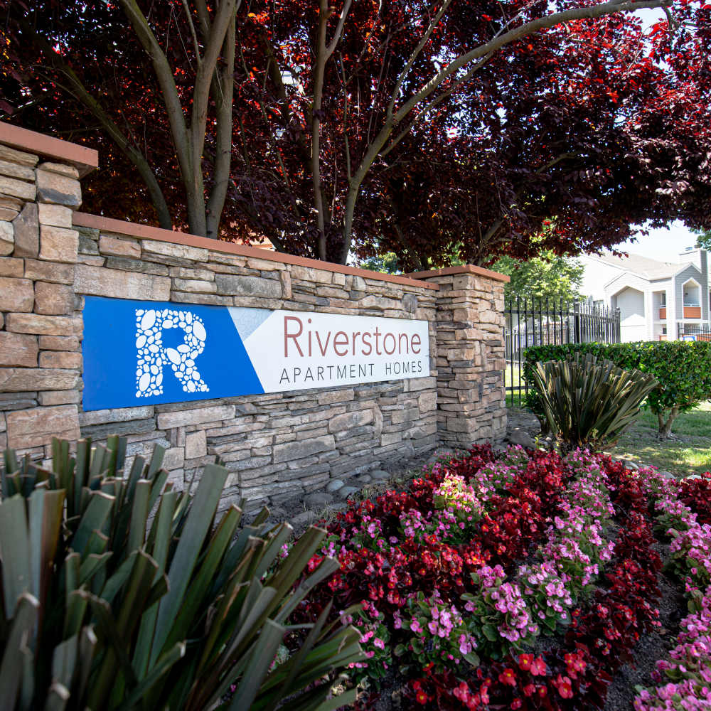 Entrance sign for Riverstone Apartment Homes, framed by vibrant red trees and stonework at Riverstone Apartments in Sacramento, California