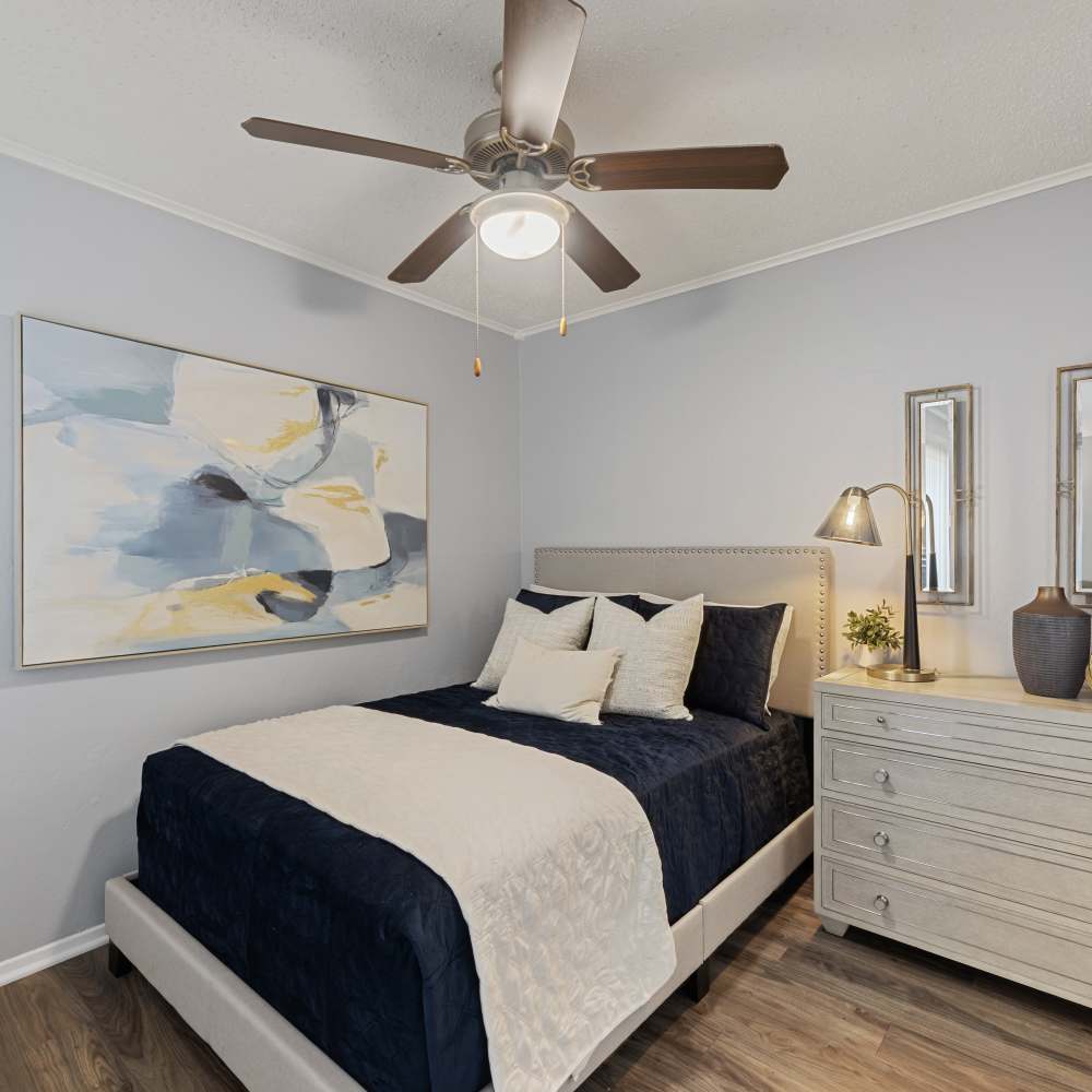 Cozy bedroom featuring a navy blue bedspread, decorative pillows, a dresser, and abstract artwork, with a ceiling fan at The Garrison in Dallas, Texas