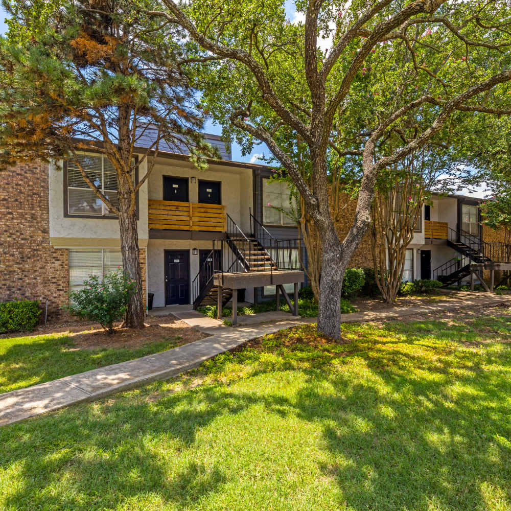 Apartment buildings with brick and gray siding exteriors, staircases, green lawns, and bright blue sky at The Garrison in Dallas, Texas