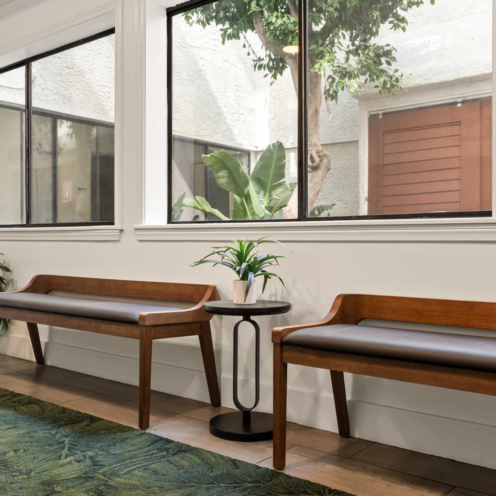 Indoor seating area with two wooden benches featuring gray cushions at Canyon Village in North Hollywood, California