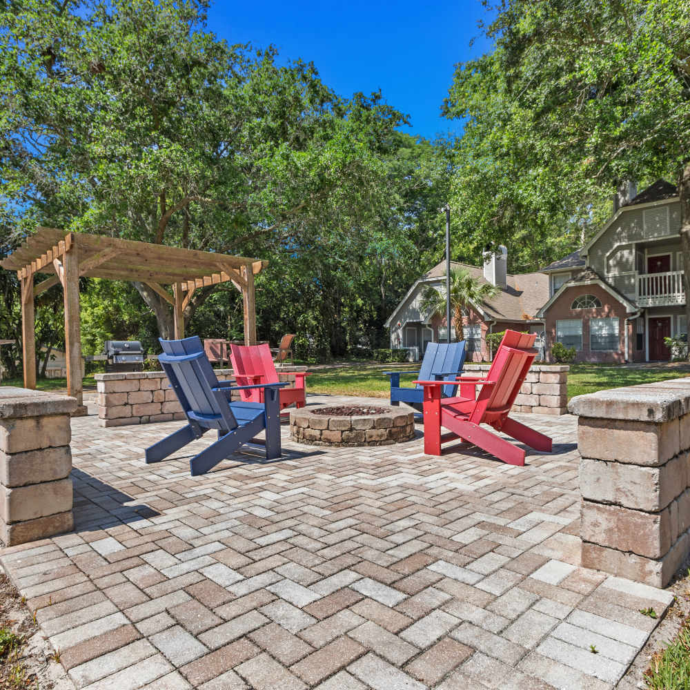 Outdoor firepit area with red and blue Adirondack chairs and pergola surrounded by trees at Twin Lakes, Palm Harbor, Florida