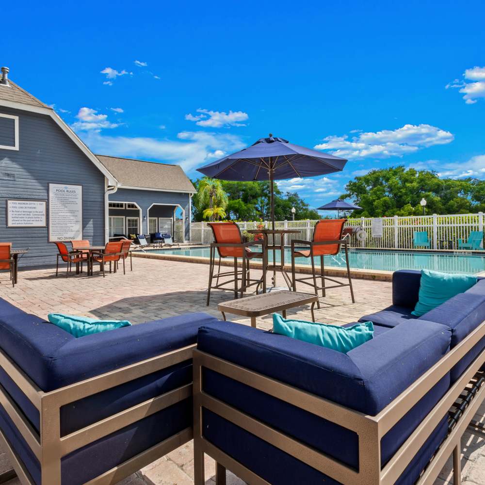 Outdoor lounge seating with blue cushions beside pool and shaded tables under sunny skies at Twin Lakes, Palm Harbor, Florida