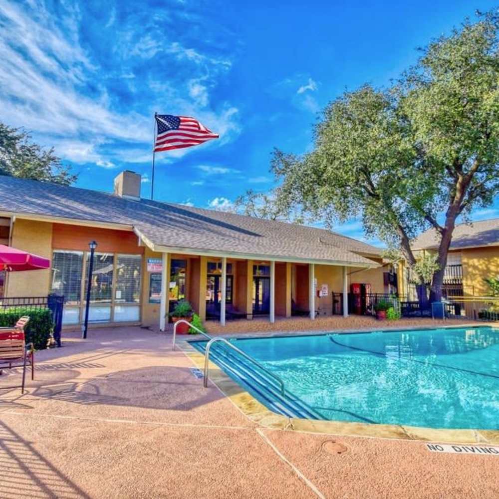 Sparkling pool surrounded by lush greenery and sunlit clubhouse at Woodlands of Plano in Plano, Texas