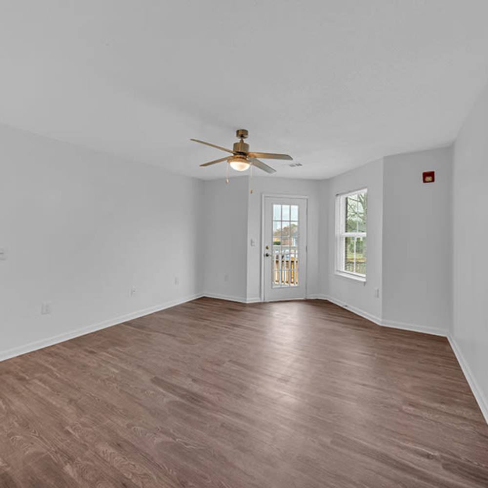 Unfurnished living room dark wood flooring, ceiling fan, large windows, and access to patio at Osprey Place Apartments in North Charleston, South Carolina