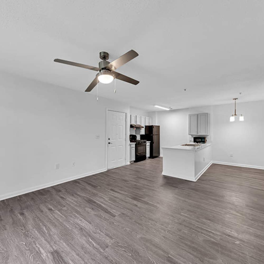 Modern apartment with open kitchen, white cabinets, island counter, dark wood flooring, and ceiling fan in living area at Osprey Place Apartments in North Charleston, South Carolina