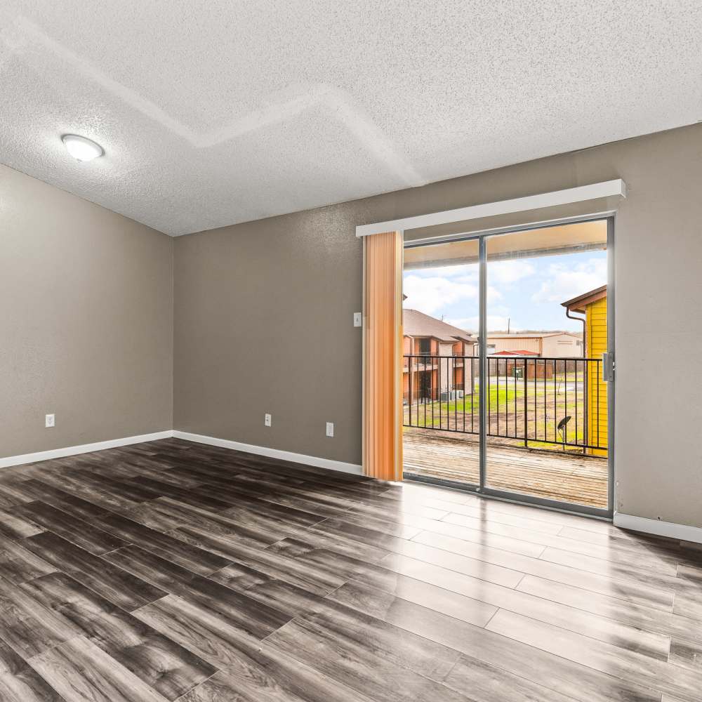 Spacious living area with wood-style flooring and sliding glass door to private balcony at Towne East Village Apartment Homes in Converse, Texas