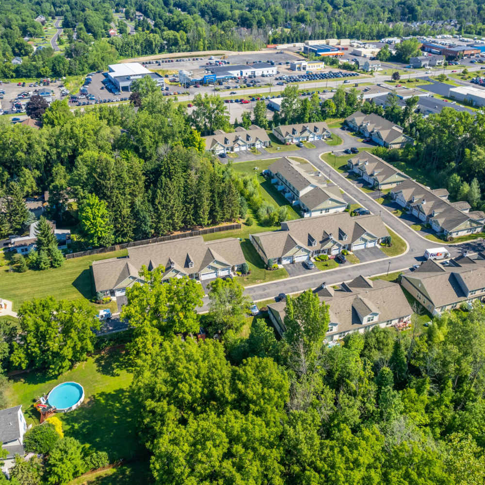 Aerial view of apartment community with green landscaping and a small pool surrounded by trees at Carriages At Cedar Rock in Webster, New York