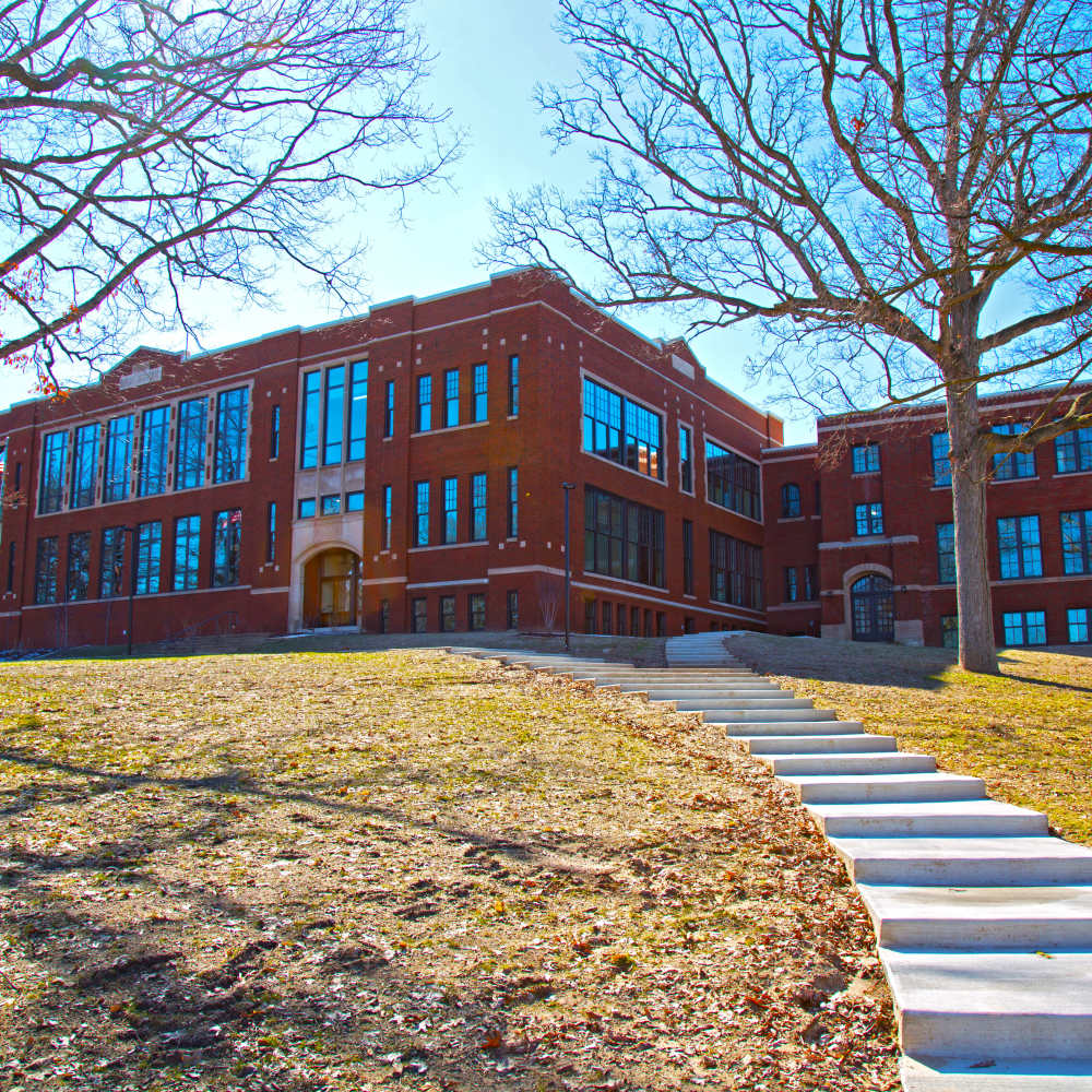Historic brick building with large windows and landscaped grounds, steps leading to the entrance at Portland School in Portland, Michigan