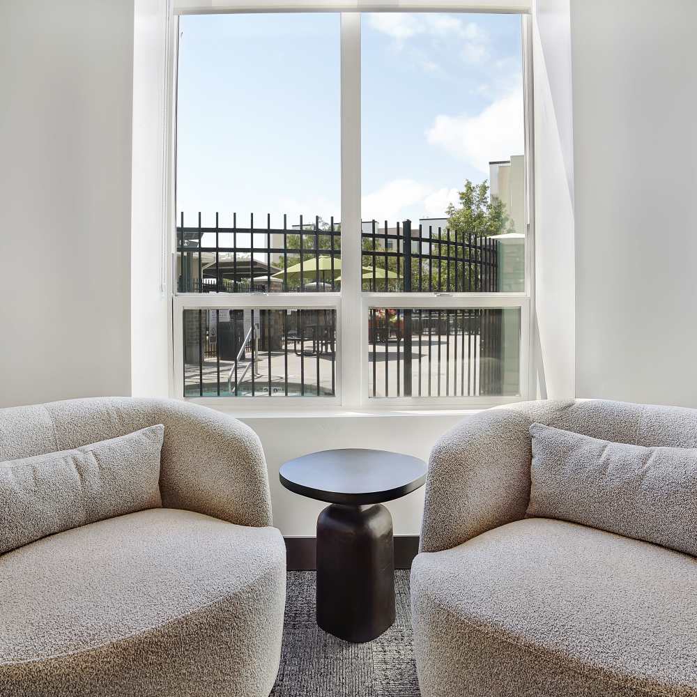 Cozy seating area with two plush chairs and a small table by a large window overlooking a gated pool area at Canyon View Crossing in Orem, Utah