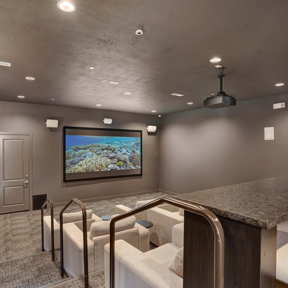 Cozy theater room with plush seating and large projection screen showcasing underwater scenery at Canyon View Crossing in Orem, Utah