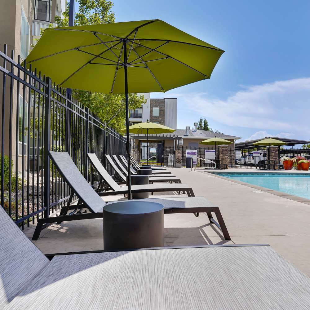 Resort-style pool area with lounge chairs and green umbrellas, gated entrance in the background at Canyon View Crossing in Orem, Utah