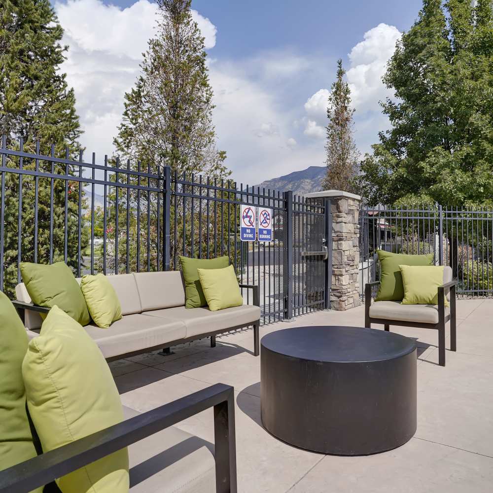 Outdoor lounge area with green cushions, circular table, and gated entrance surrounded by trees at Canyon View Crossing in Orem, Utah