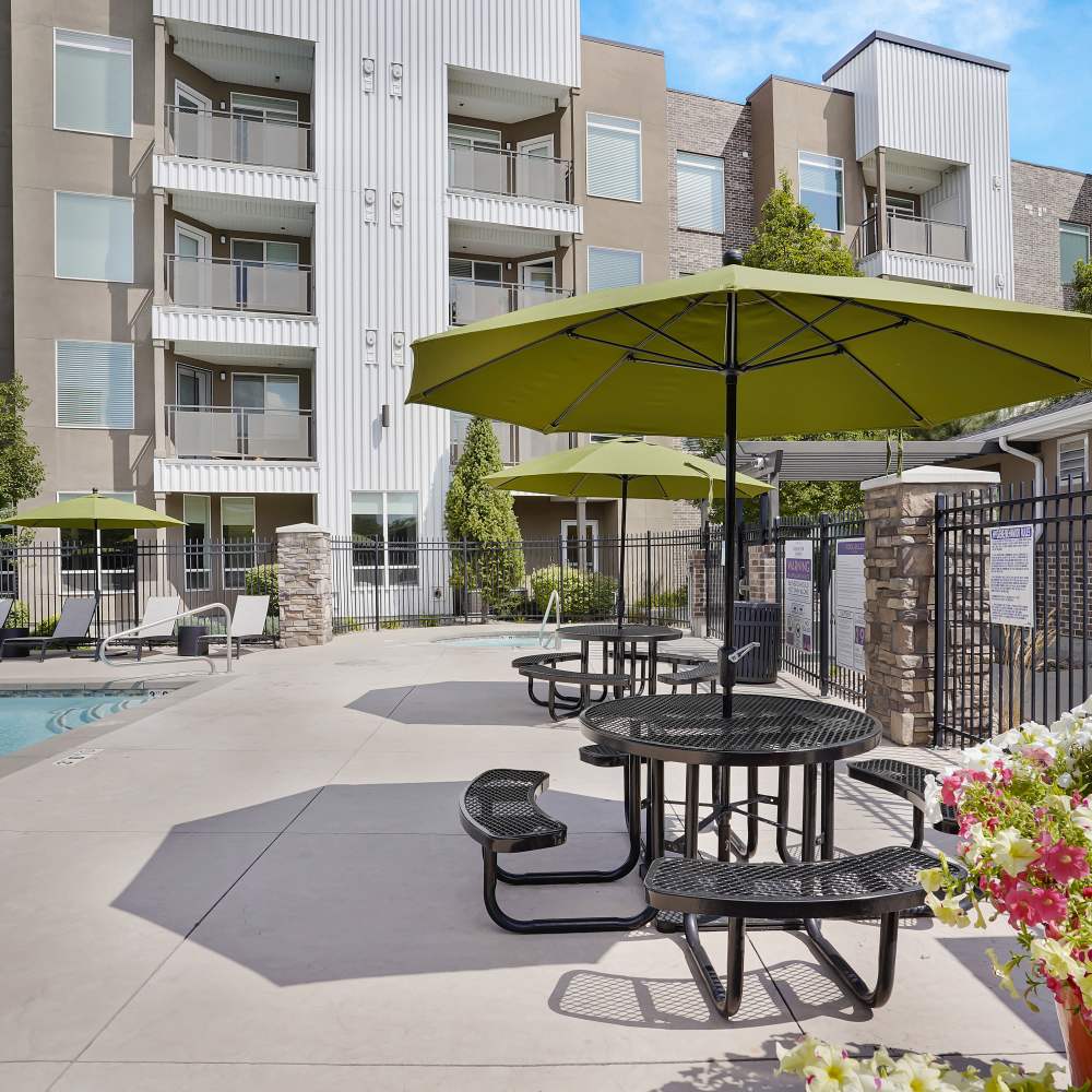 Resort-style pool area with shaded seating and vibrant flowers in a modern apartment community at Canyon View Crossing in Orem, Utah