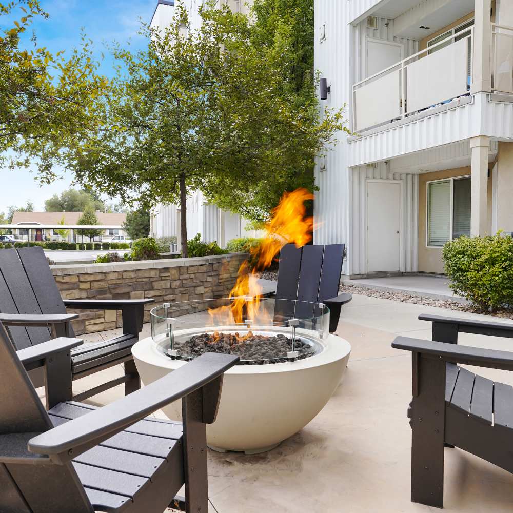 Outdoor fire pit surrounded by black Adirondack chairs and lush greenery at Canyon View Crossing in Orem, Utah