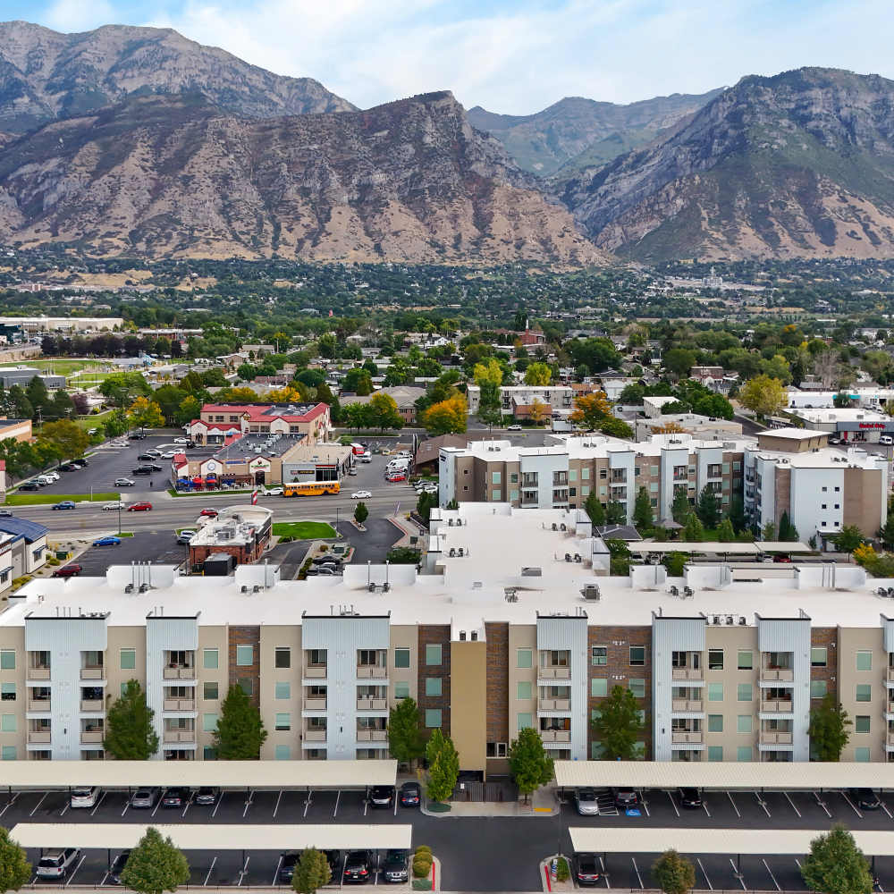 Aerial view of modern apartment community with mountain backdrop and landscaped parking area at Canyon View Crossing in Orem, Utah