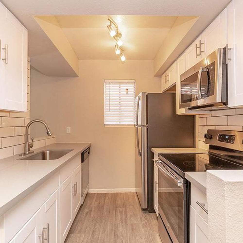 Modern kitchen with stainless steel appliances, granite countertops, and wood-style flooring at Fairways on Thunderbird in Phoenix, Arizona