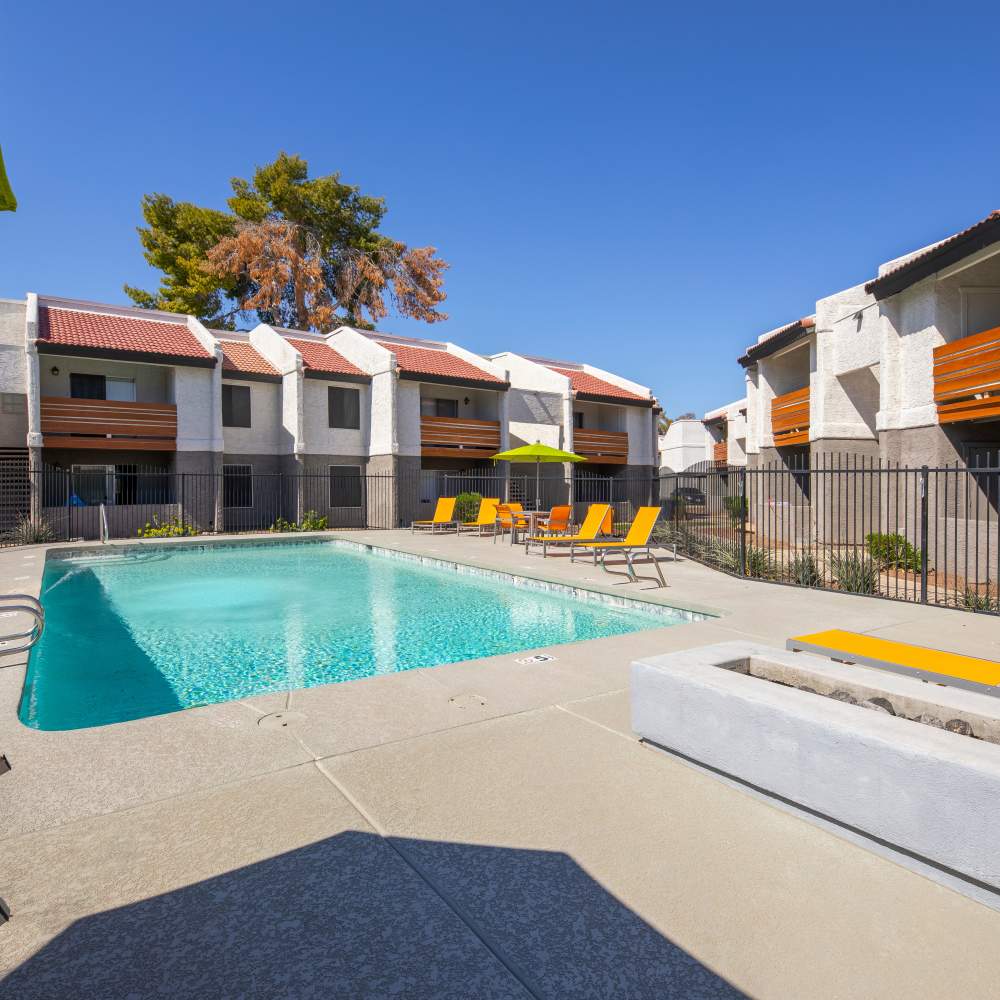 Resort-style pool surrounded by lounge chairs and vibrant umbrellas with apartment buildings in the background at Fairways on Thunderbird in Phoenix, Arizona