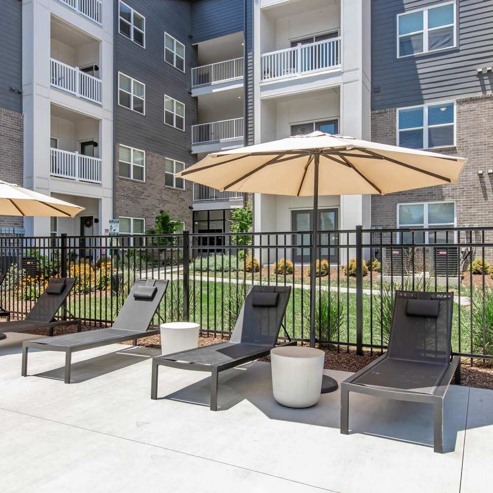 Lounge chairs under umbrellas by a gated pool area with landscaped greenery at The Arcadia in Madison, Tennessee
