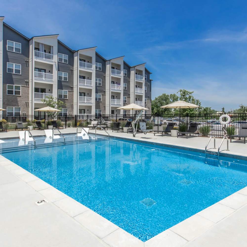 Sparkling pool surrounded by lounge chairs and umbrellas with modern apartment buildings in the background at The Arcadia in Madison, Tennessee