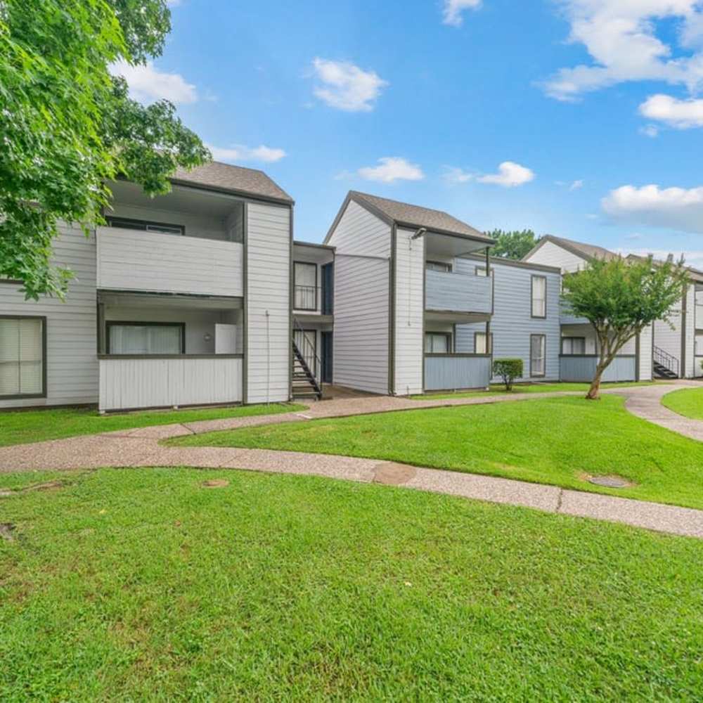 Apartment buildings with balconies, lawn, and curved walkway path at The Montclair in Houston, Texas