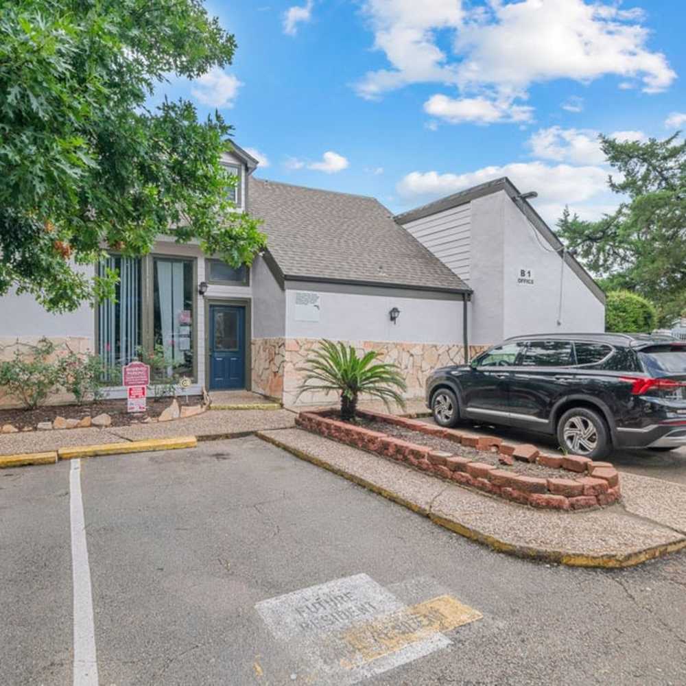 Leasing office exterior with parking spaces, cars, and entry walkway at The Montclair in Houston, Texas