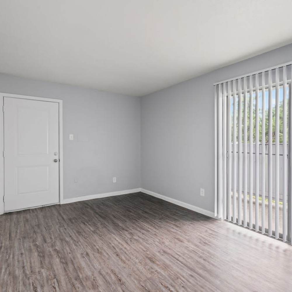Empty living room with wood-style flooring, white door, and patio sliding glass doors at The Montclair in Houston, Texas