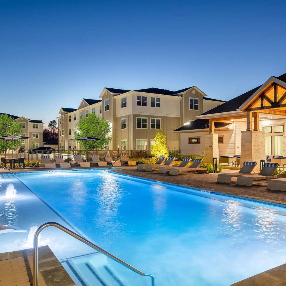 Sparkling pool with lounge chairs at night at August Friendswood in Friendswood, Texas