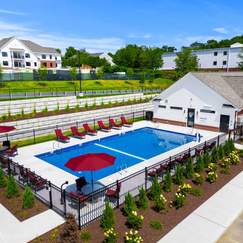Aerial view of community swimming pool with lounge chairs and landscaping at Middleborough Station in Middleborough, Massachusetts