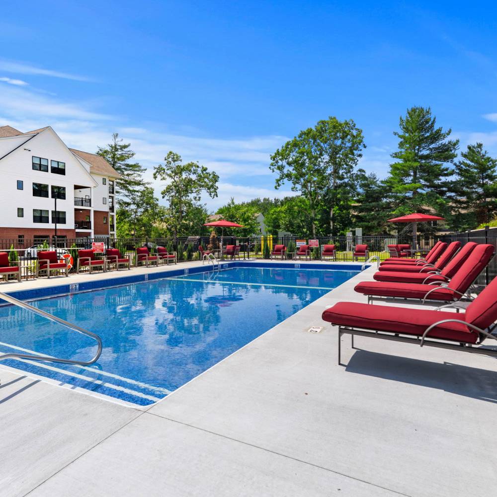 Resort-style outdoor pool with cushioned loungers and apartment buildings at Middleborough Station in Middleborough, Massachusetts