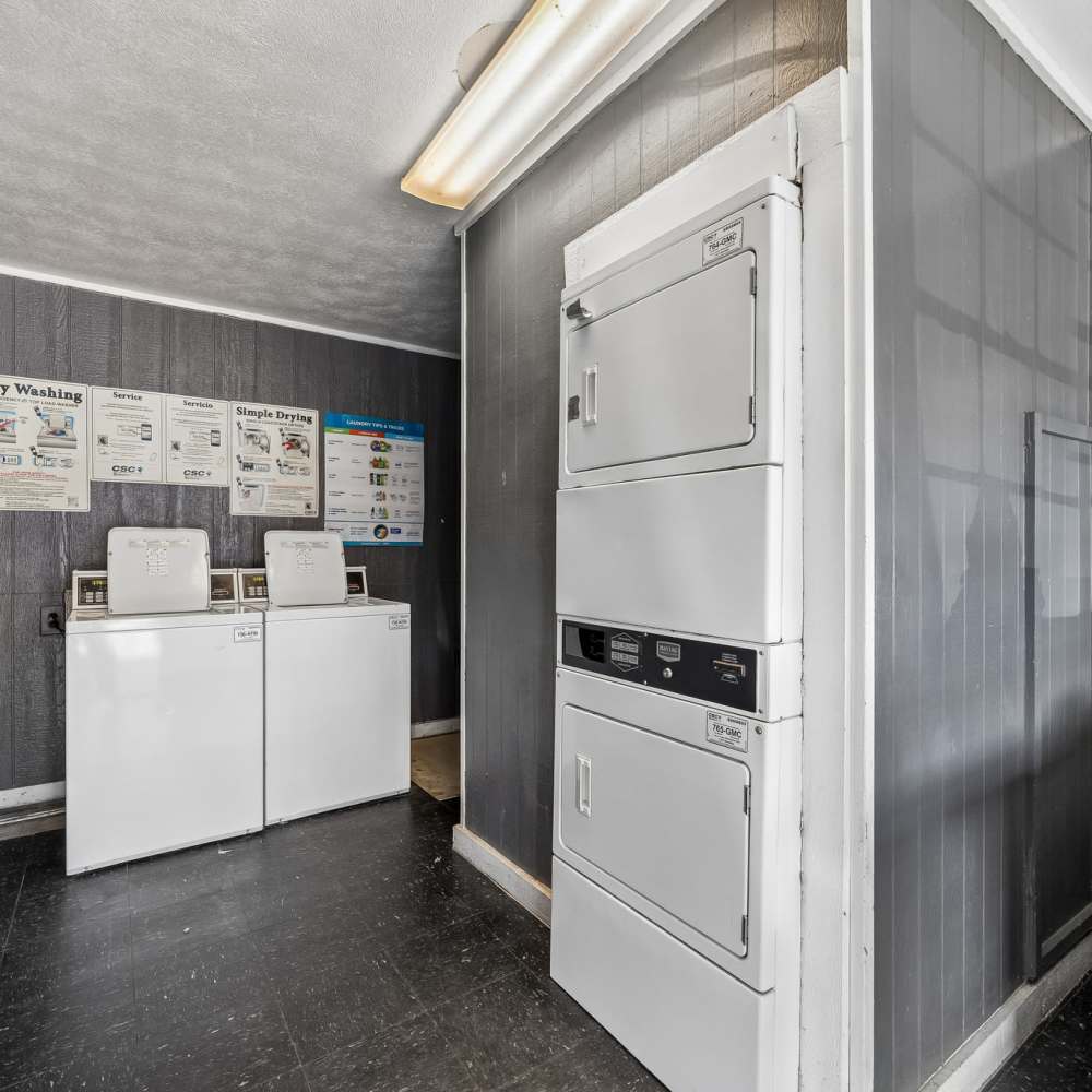Shared laundry room with white washers and stacked dryers, washing instructions on the wall, and a red fire extinguisher; clean, utilitarian setting at Royal Arms in Richardson, Texas