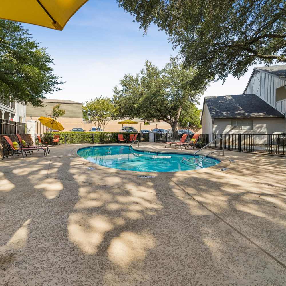 Sunny apartment courtyard with turquoise swimming pool, lounge chairs, shade trees, umbrellas, and balconies creating a peaceful retreat at Royal Arms in Richardson, Texas