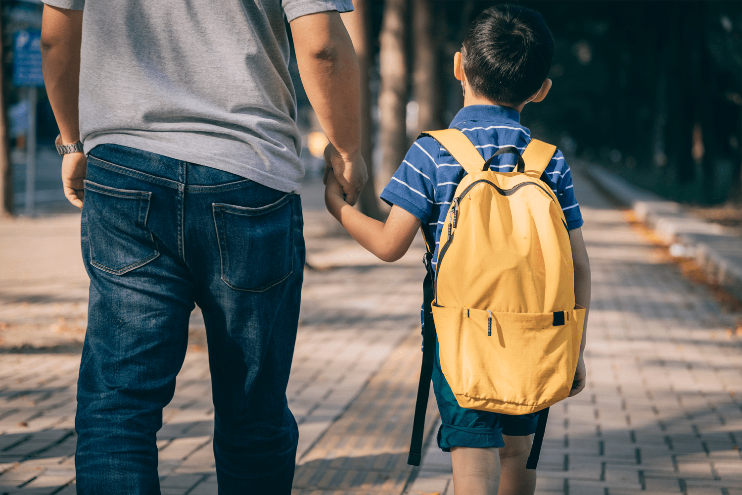 Parent holding hands with a child wearing a yellow backpack
