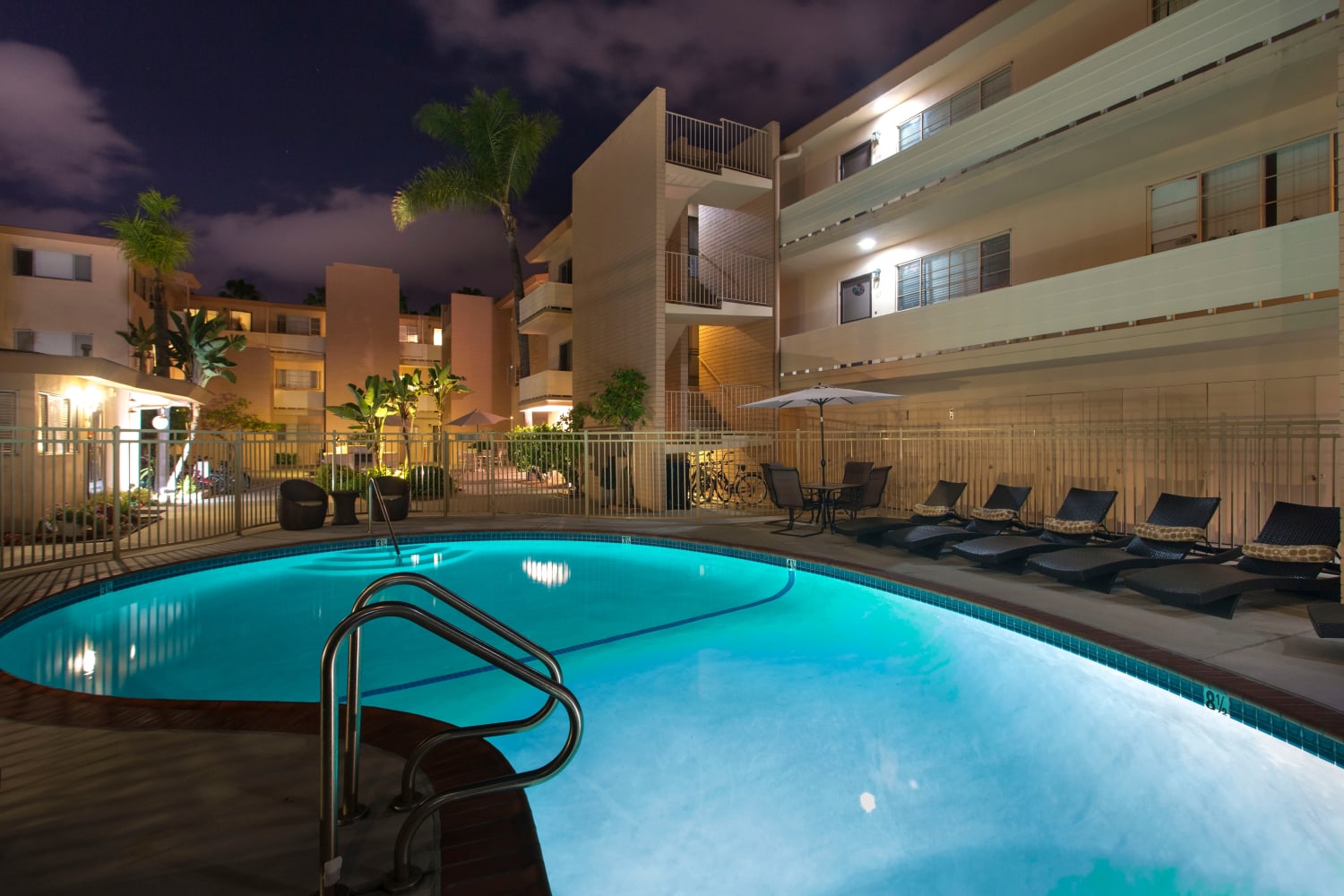 Pool at night with palm trees and lounge chairs at Emerald Manor Apartments in San Diego, California