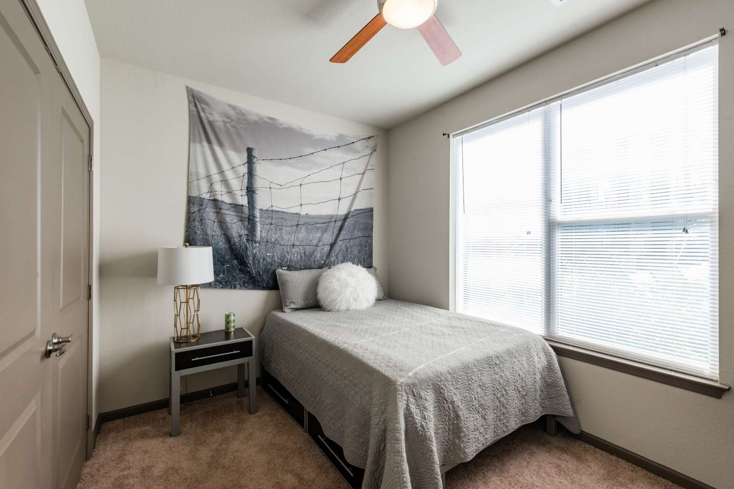 Carpeted bedroom with sunlit window and ceiling fan at The Quarters at Stillwater in Stillwater, Oklahoma