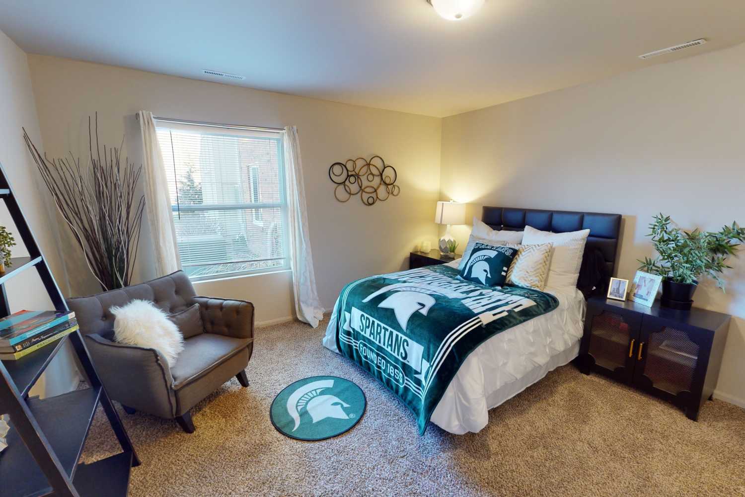 Large apartment bedroom with full-size bed and accent chair at The Quarters at East Lansing in East Lansing, Michigan