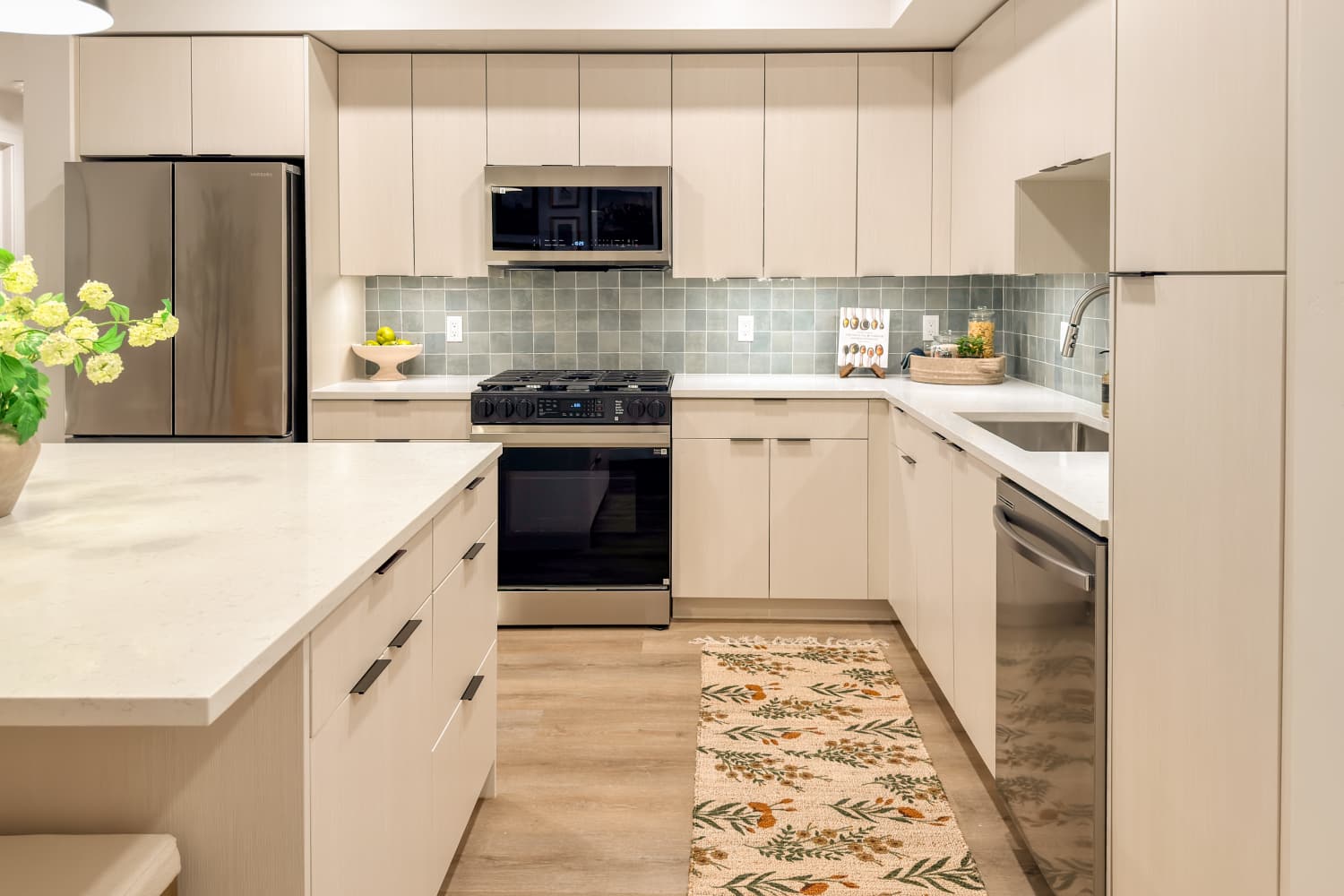 Modern kitchen with light wood cabinets, stainless steel stove and fridge, green tile backsplash, and a narrow patterned rug at RIVA Solana Beach in Solana Beach,California