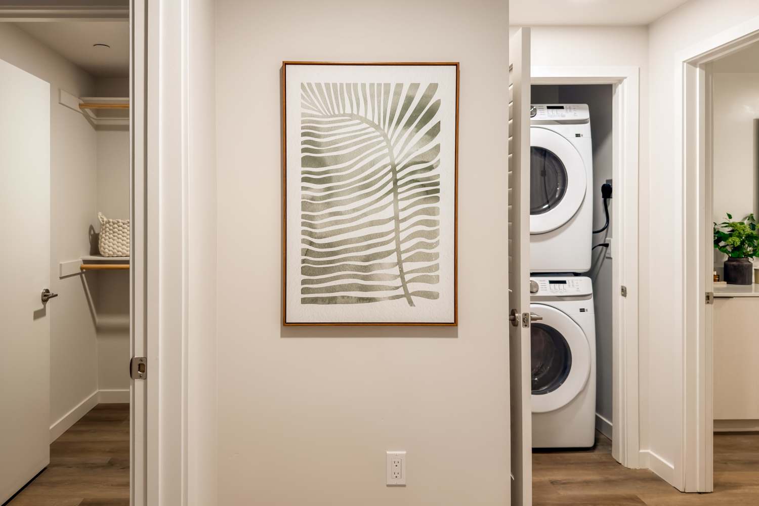 Hallway with framed wall art, open closet door, and stacked washer and dryer in a laundry nook at RIVA Solana Beach in Solana Beach,California