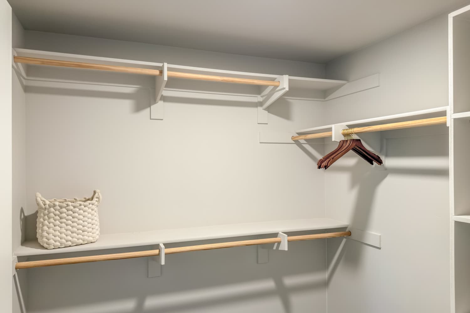Walk‑in closet with white shelving, hanging rods, woven baskets, and wood‑look flooring at RIVA Solana Beach in Solana Beach,California