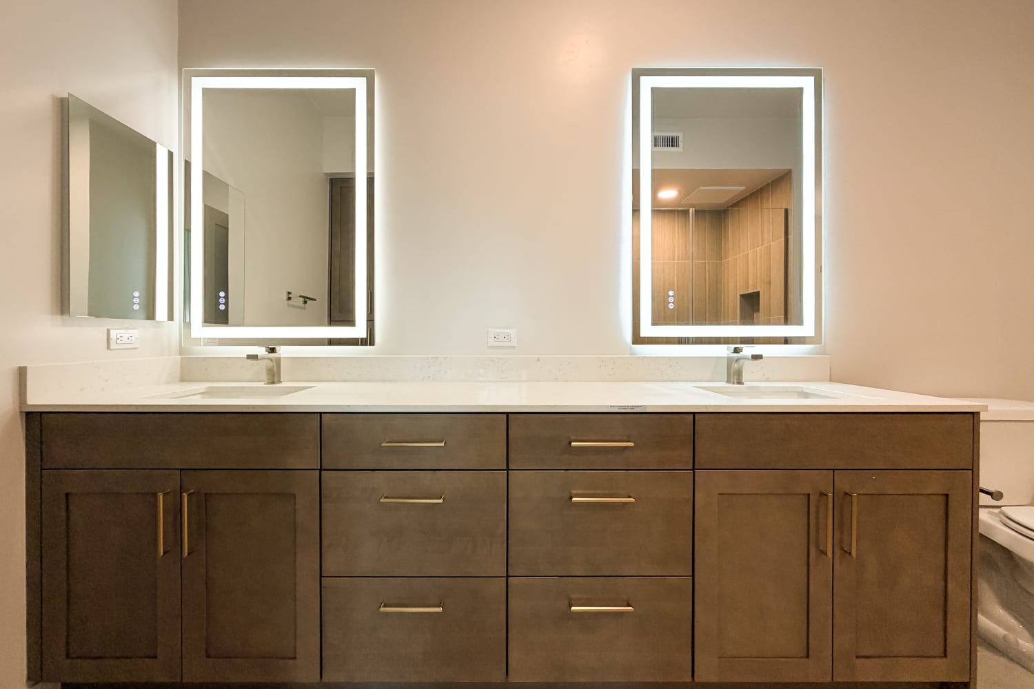Double‑sink bathroom vanity with dark wood cabinets, white countertop, and two illuminated mirrors at RIVA Solana Beach in Solana Beach,California