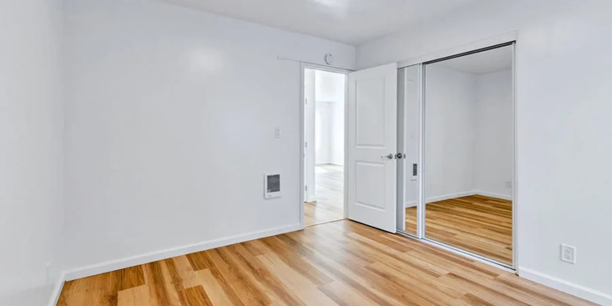 An apartment bedroom with wood flooring and a mirror on the closet door at Silverado Gardens in Napa, California