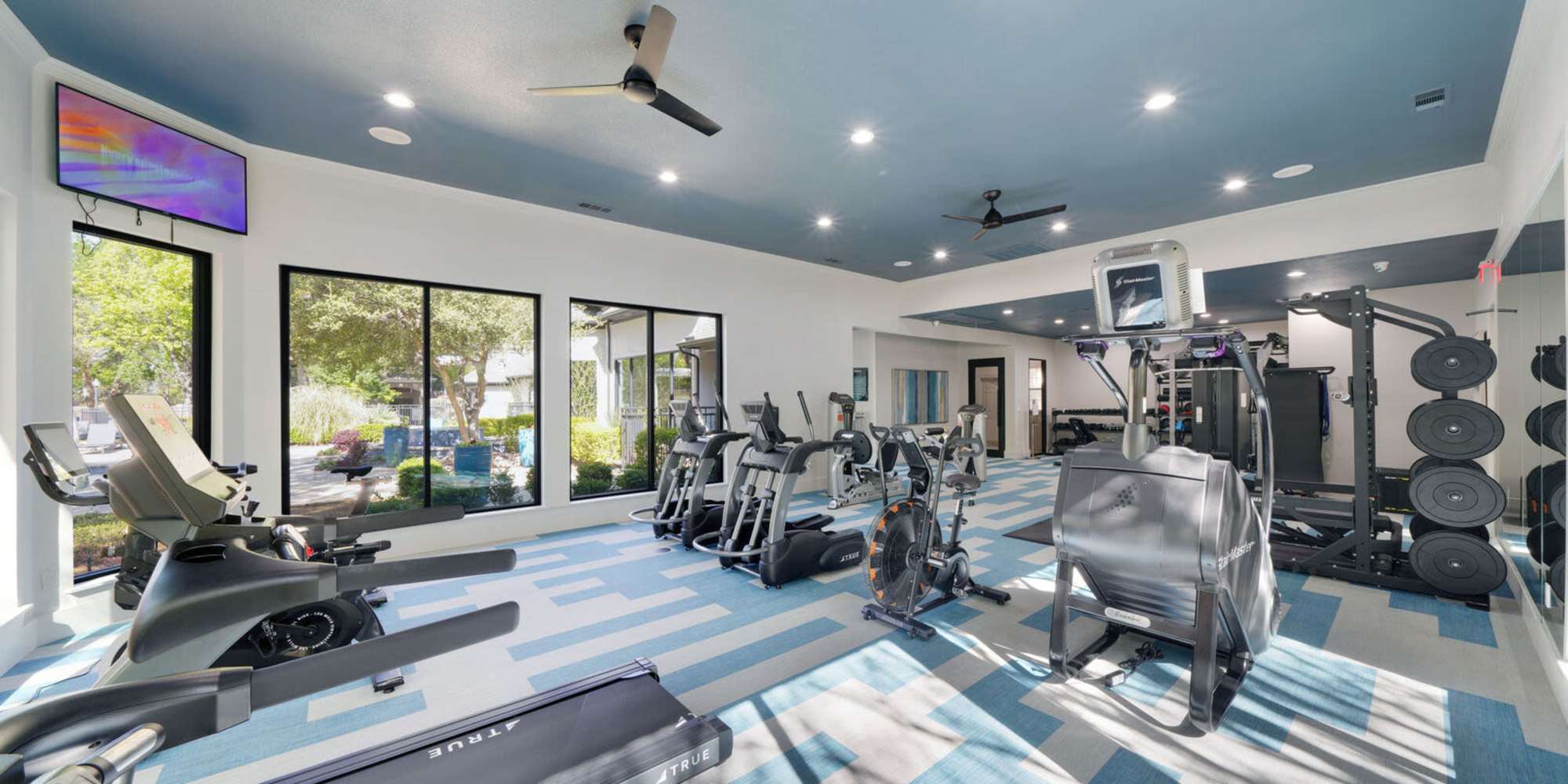Fully-equipped gym with treadmills, flat-screen TVs, and ceiling fans at St. Martin in Frisco, Texas, 