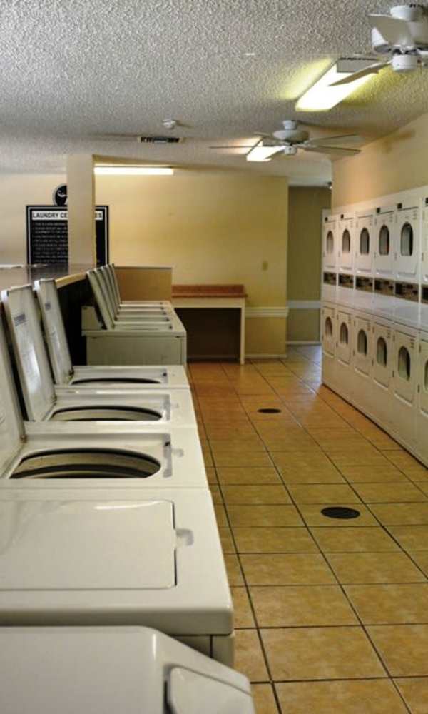 A long, well-lit laundry room with rows of stacked white washing machines and dryers at The Abbey At Northlake in Riviera Beach, Florida