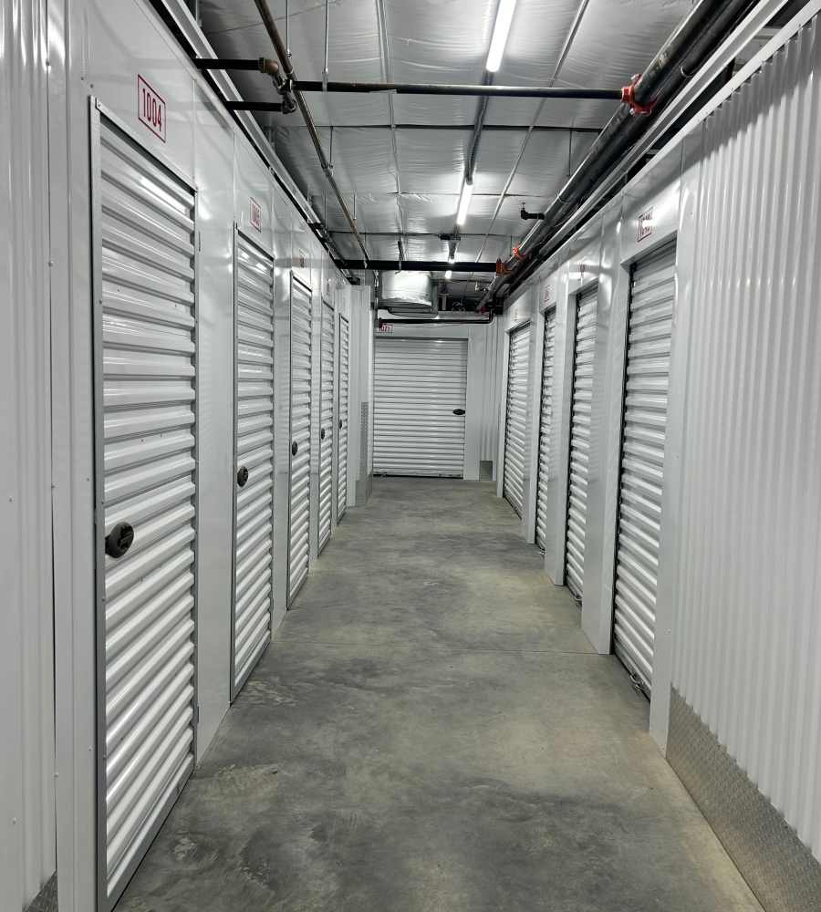 Interior hallway of storage units with bright lighting and concrete flooring at Storage Authority Carolina Road in Suffolk, Virginia