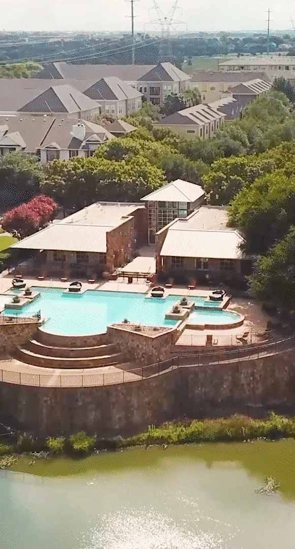 Aerial view of a large pool next to a house with a lush garden at Flatiron District at Austin Ranch, The Colony, Texas