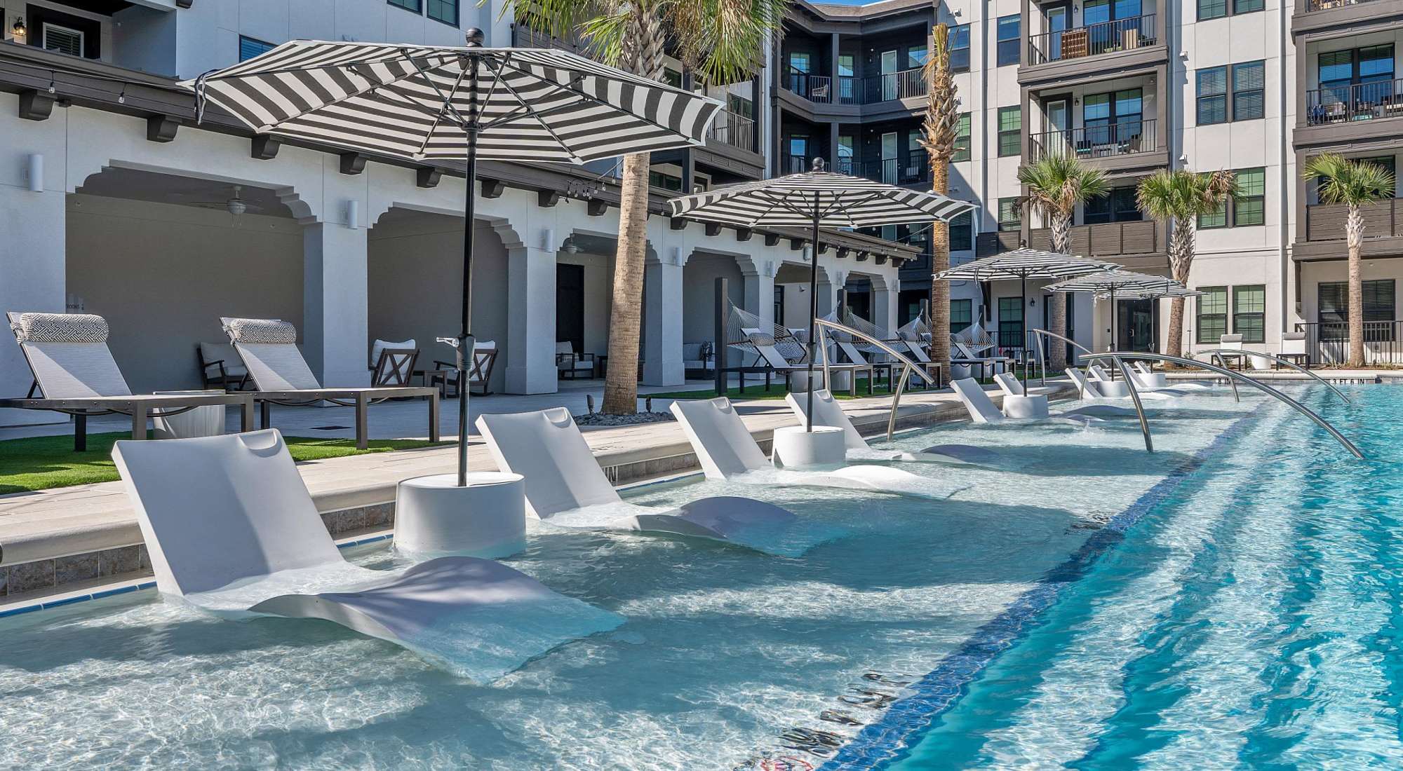 Resort-style swimming pool with in-pool lounge chairs at Palmilla | Luxury Apartments & Townhomes in Pensacola, Florida
