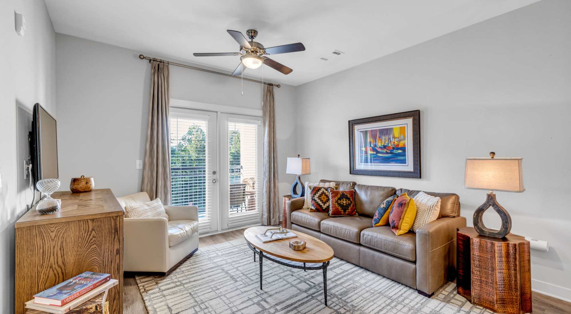 A Living Room With A Brown Leather Couch, White Armchair, And Balcony Access. at Artessa in Franklin, Tennessee