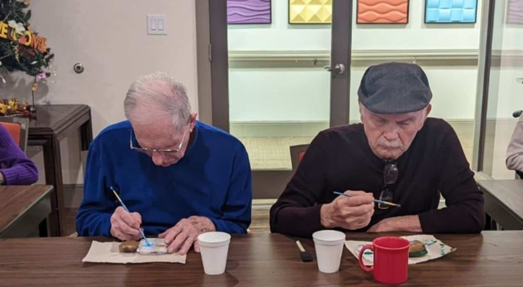 Two senior men relaxing in cozy chairs while painting and having coffee.