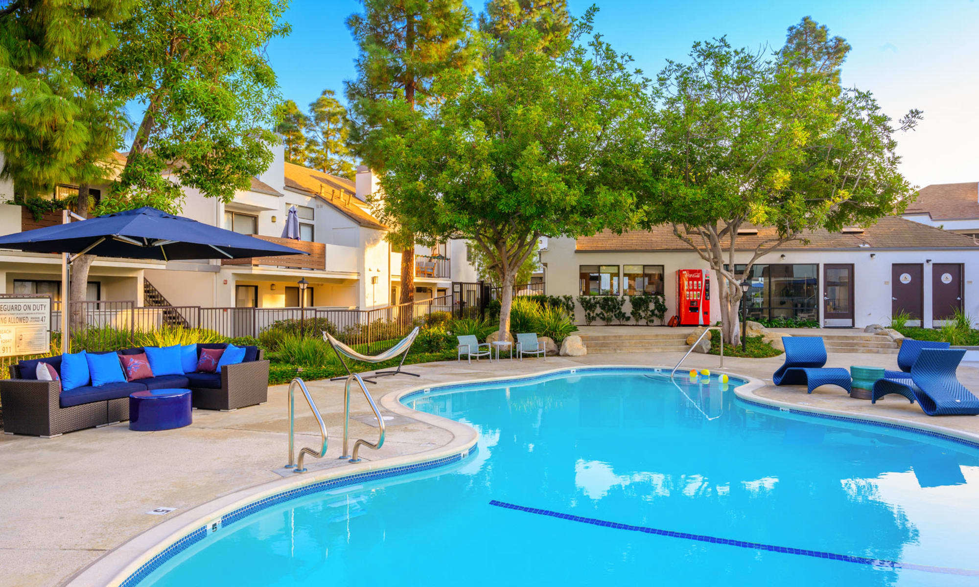 Shaded lounge areas near the swimming pool surrounded by mature trees at Pleasanton Place Apartment Homes in Pleasanton, California