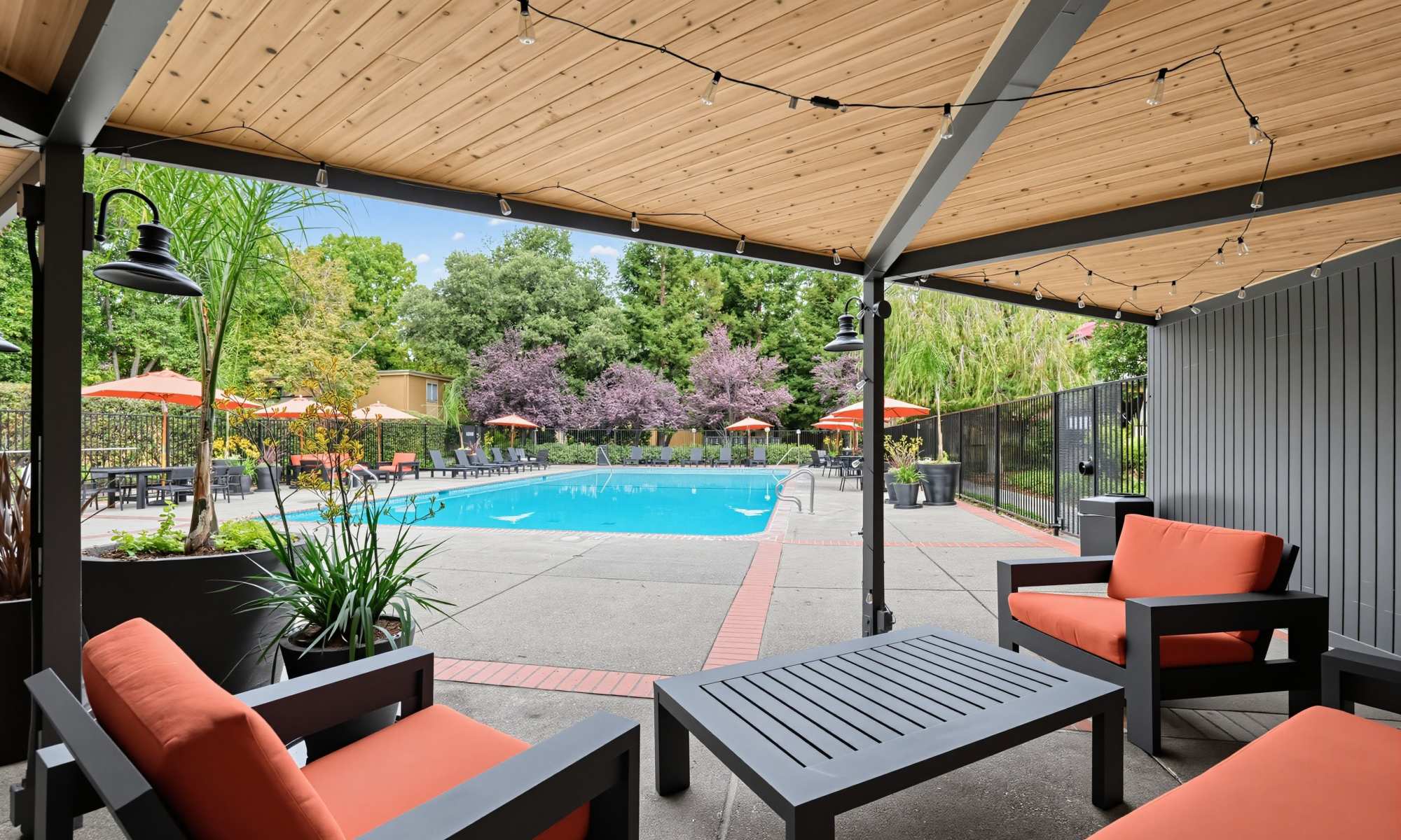 Covered patio with orange lounge seating overlooking the pool at Greenpointe Apartment Homes in Santa Clara, California