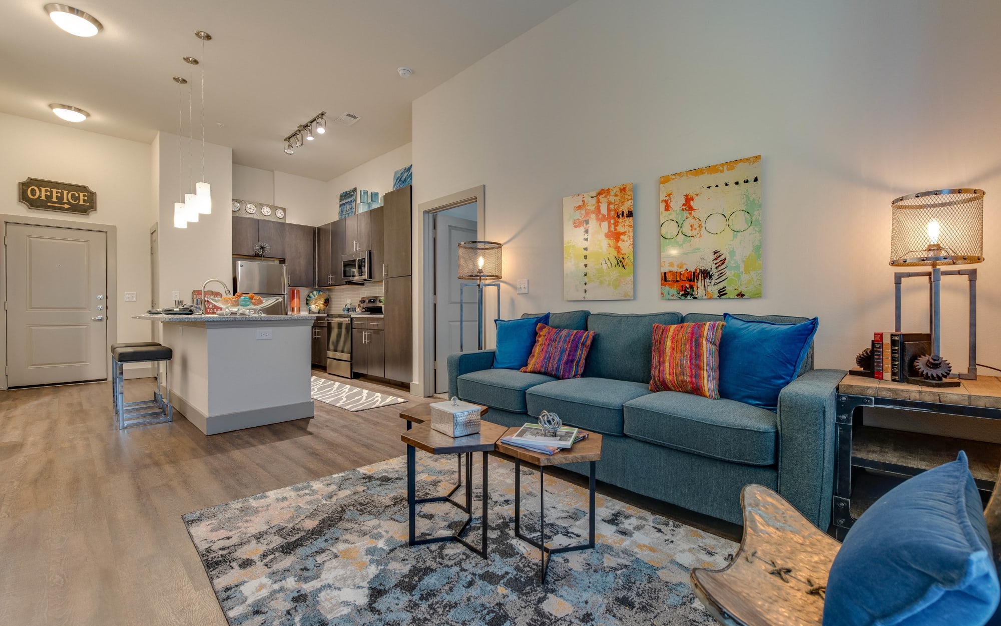 Furnished apartment living room with large area rug and blue sofa with coffee table at Bellrock Market Station in Katy, Texas